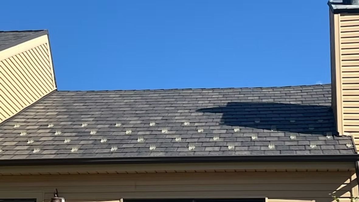 Part of a roof with gray shingles, against a clear blue sky.