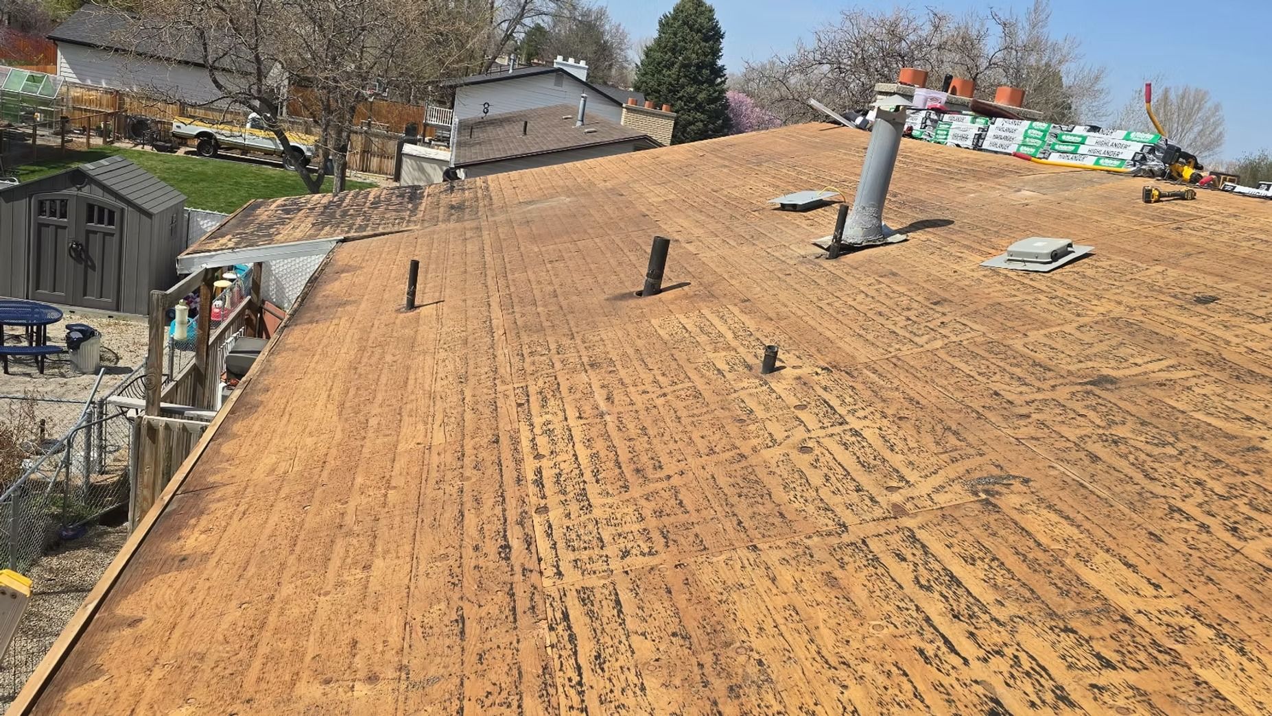 Rooftop with old roofing removed, showing wooden boards and several vents. Daytime, outdoor setting.