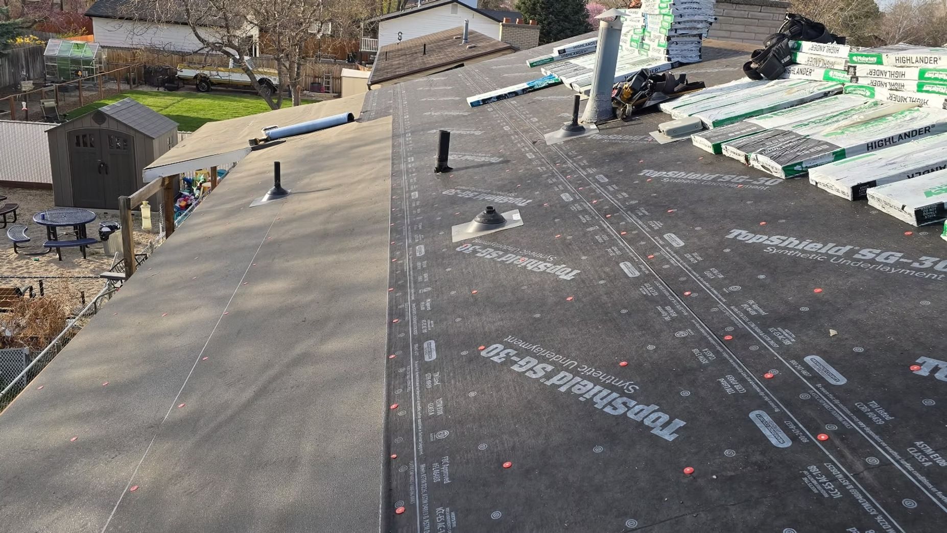 Roofing work in progress; black underlayment on roof, shingles and materials stacked.