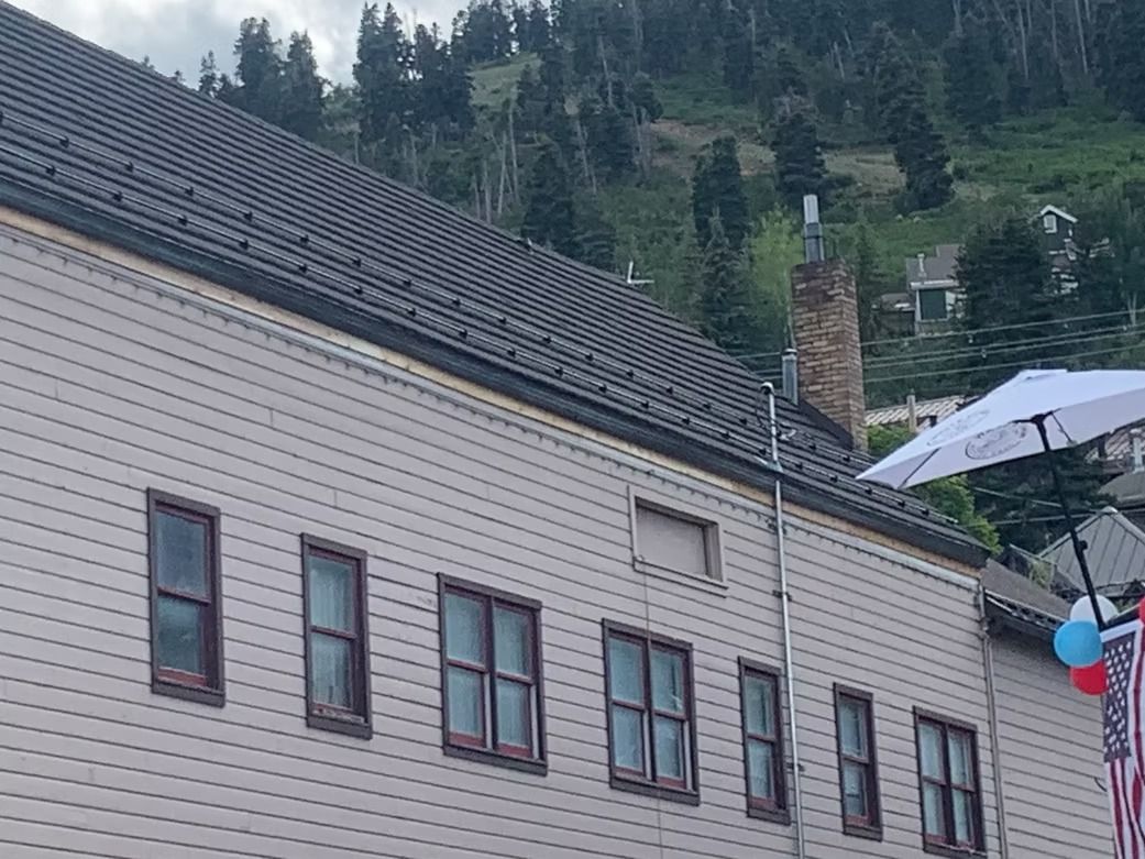Building with multiple windows, angled roof, chimney. White exterior, dark window frames. Mountain backdrop.