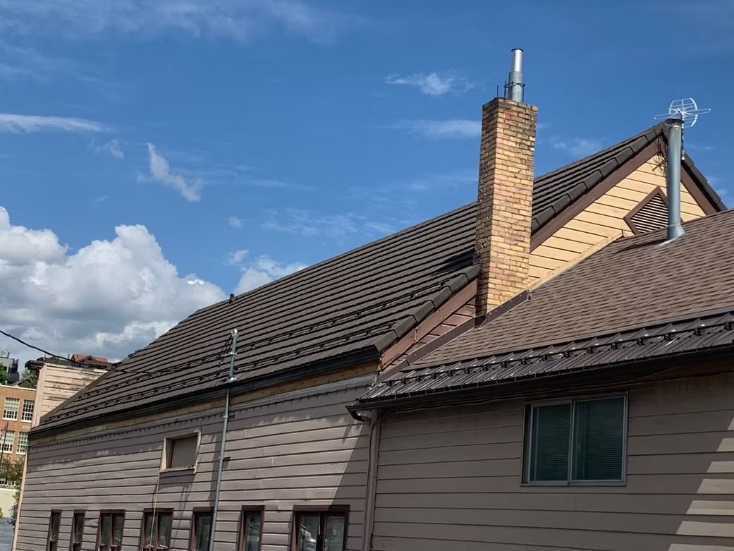 Buildings with brown tiled roofs, brick chimney against blue sky with clouds.