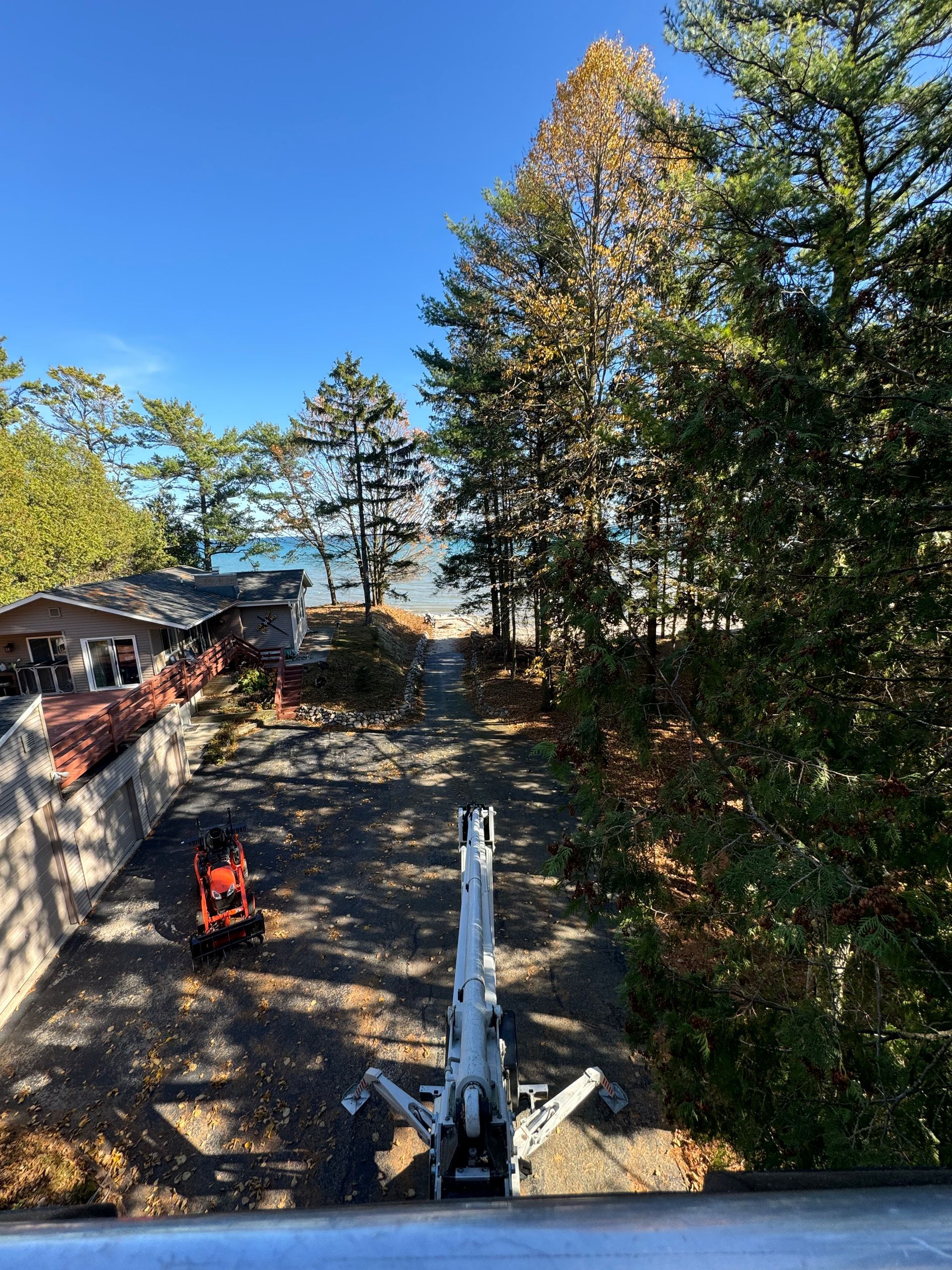 View from above of a tree-lined driveway leading to a beach. An orange tractor and a boom lift are visible.