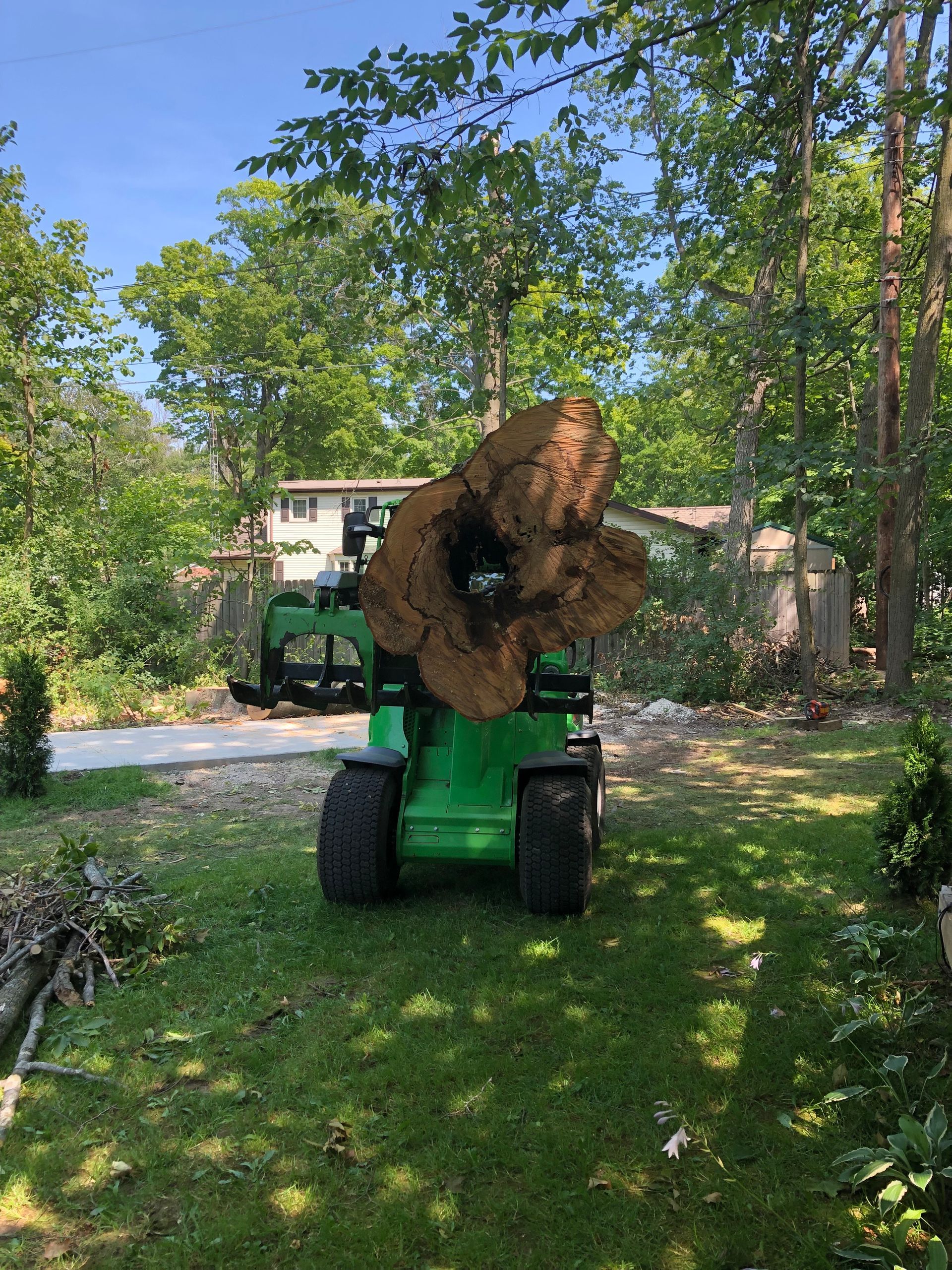 Green loader carrying a large tree trunk in a residential yard.