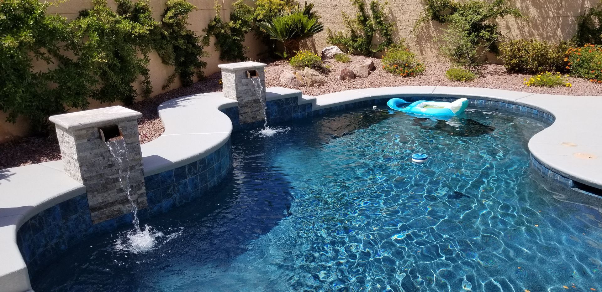 A swimming pool with a blue raft in it and a waterfall.