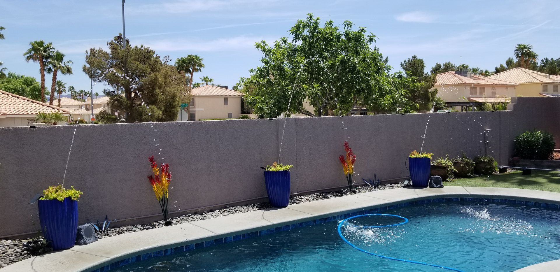 A swimming pool is surrounded by potted plants and a fence.