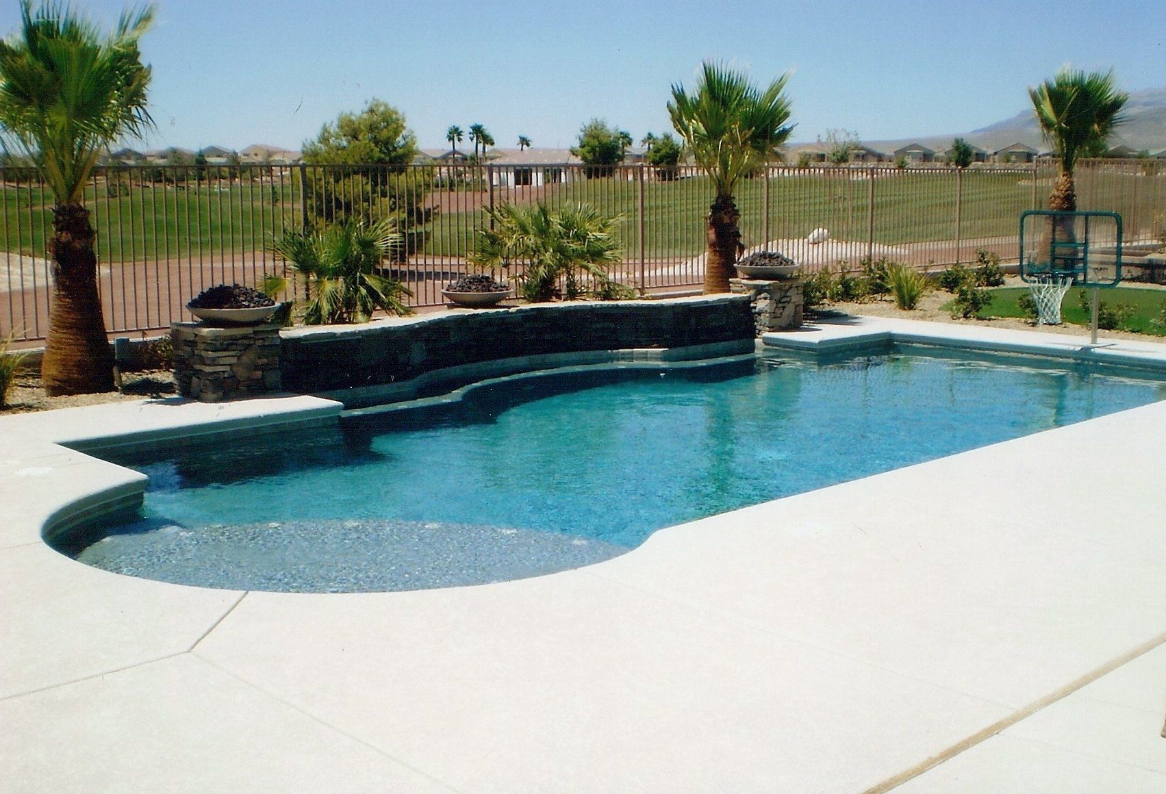 A large swimming pool surrounded by palm trees and a fence