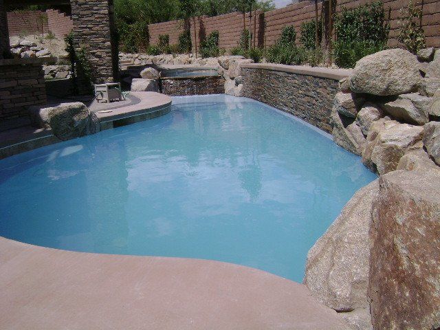 A large swimming pool surrounded by rocks and a stone wall