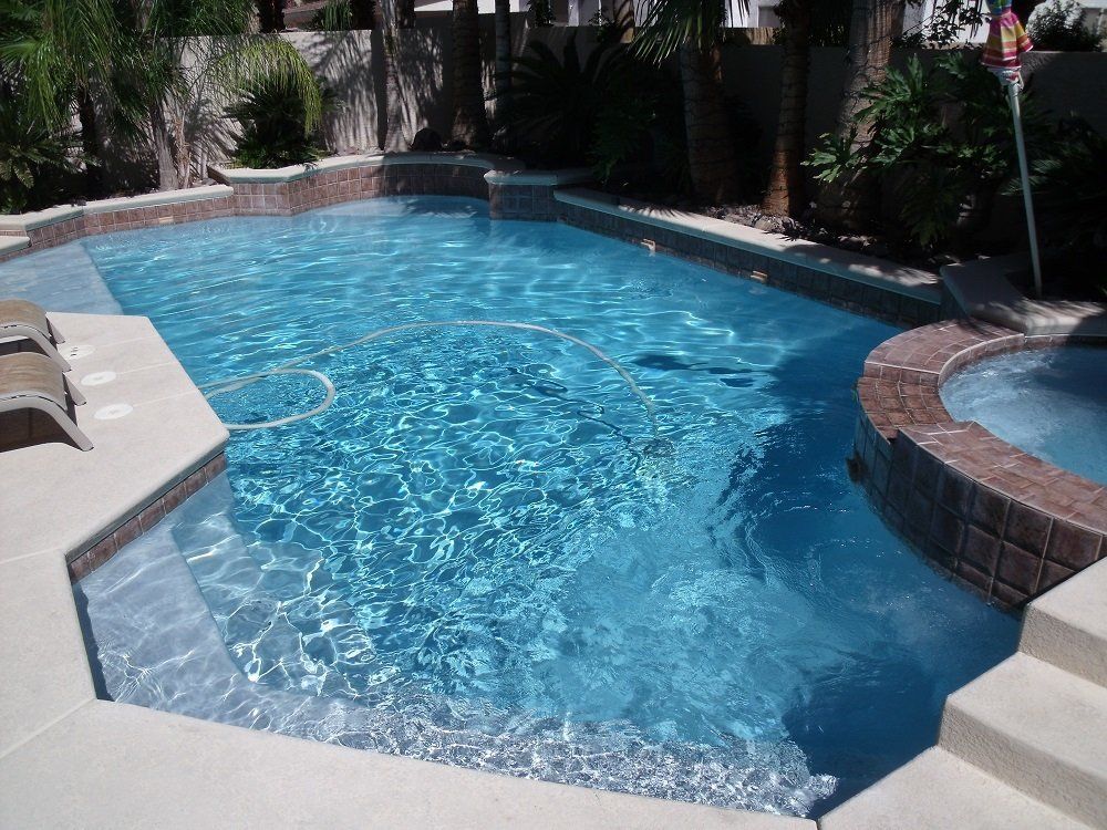 A large swimming pool with a hot tub in the backyard