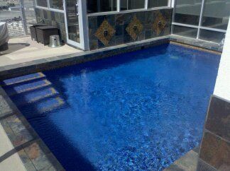 A large blue swimming pool is sitting on top of a patio next to a building.