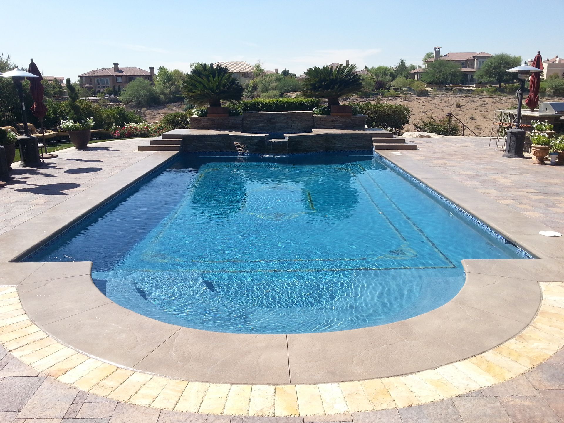 A large swimming pool is surrounded by patio furniture and umbrellas