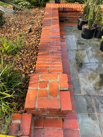 Red brick retaining wall next to a stone walkway and garden with small pebbles.
