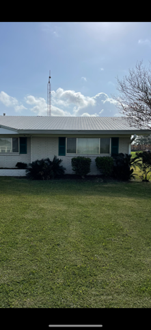 A house with a green lawn under a partly cloudy sky. There's a tall antenna in the background.