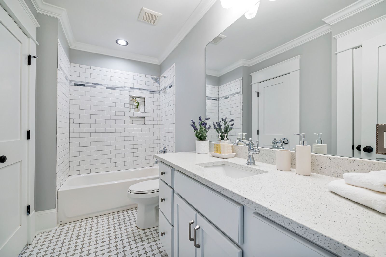 A bright, modern bathroom with a white vanity, a bathtub with white subway-style tile, and a geometric-patterned floor.