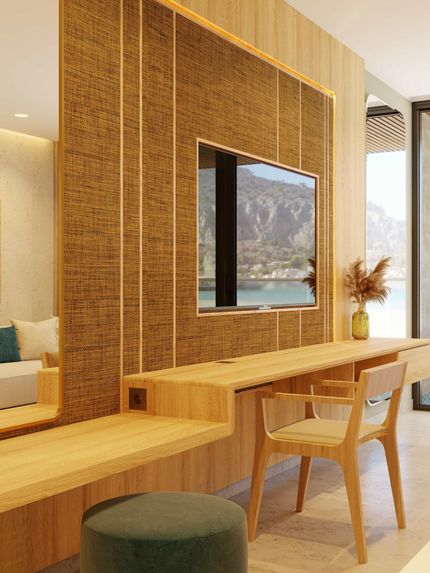 A modern hotel room with wooden desk, TV, mirror, and chair, overlooking a scenic view.