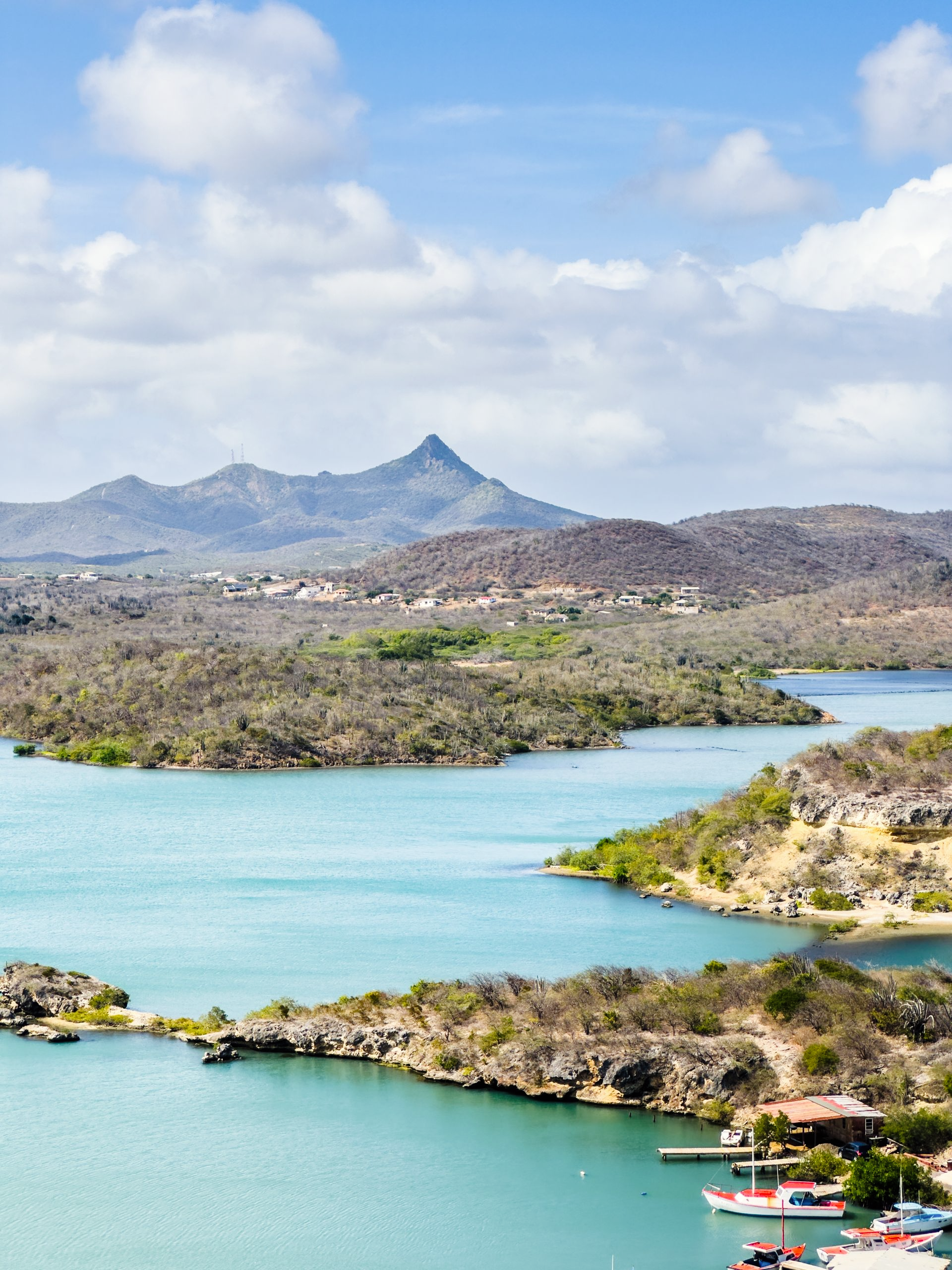 Turquoisekleurige baai met rotsachtige kustlijn en dor landschap onder een gedeeltelijk bewolkte hemel.