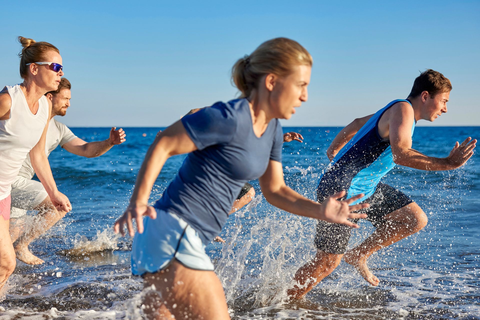 People running in the ocean, splashing water. Sunny day, blue water and sky.