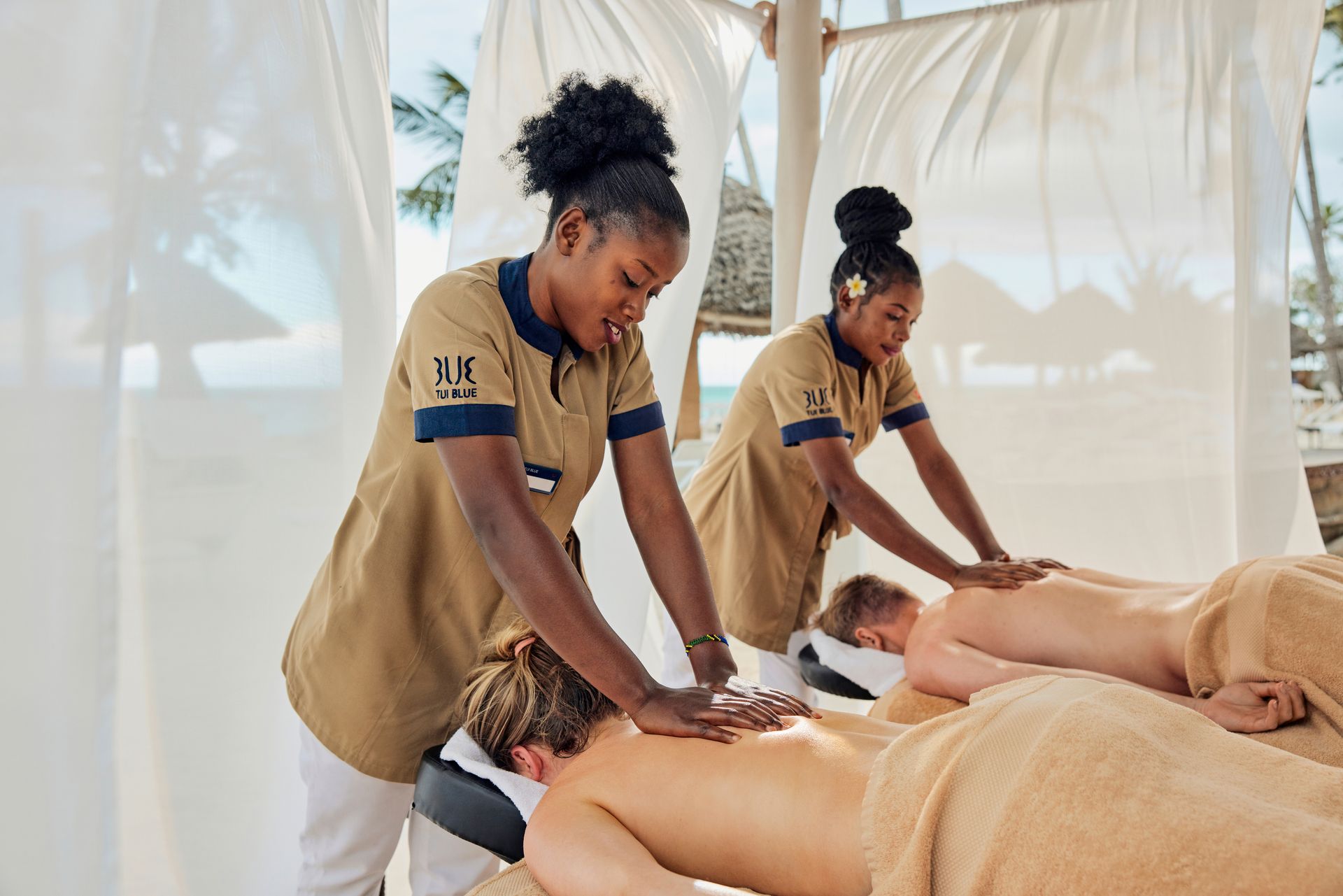 Two spa therapists giving massages to two people on outdoor massage tables.