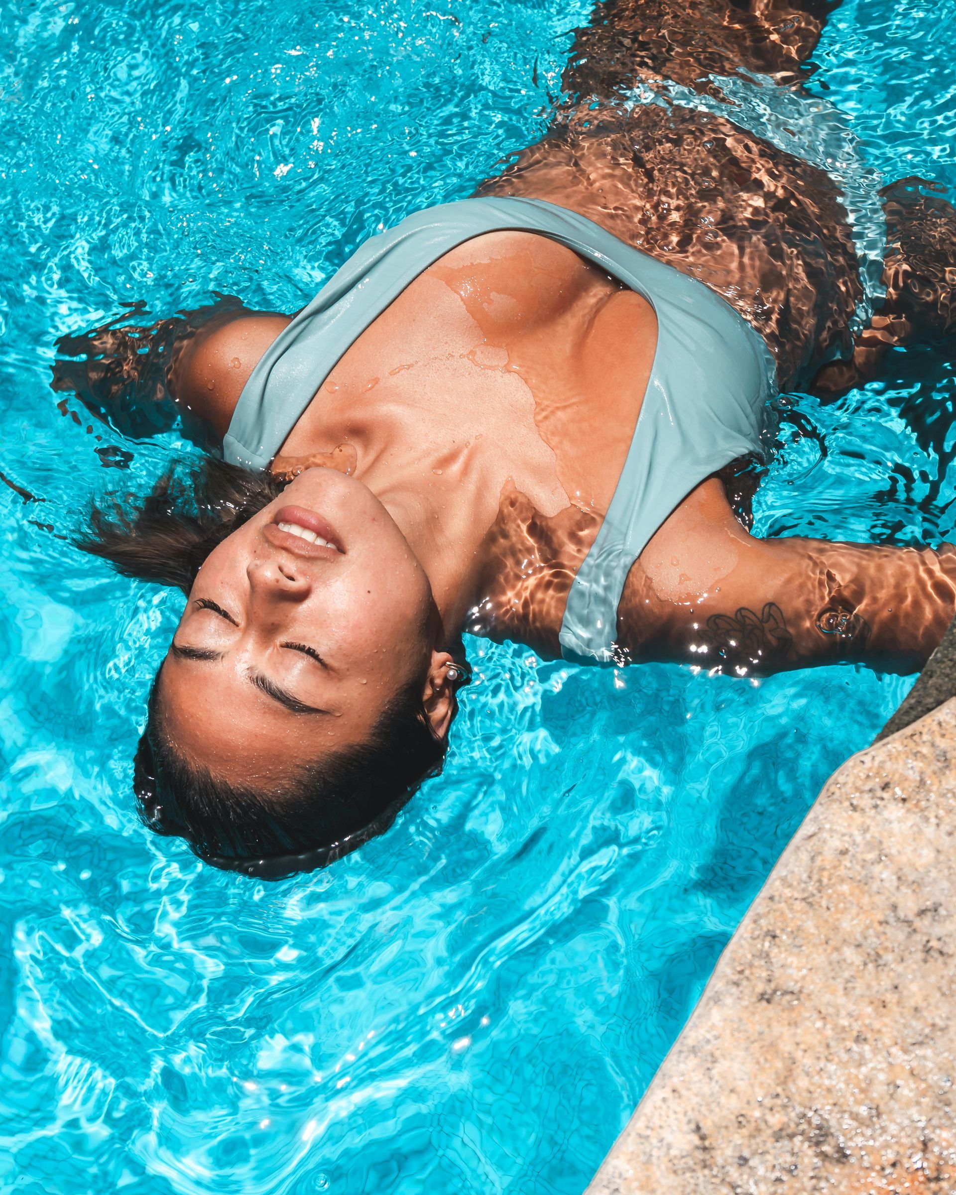 Woman in blue swimsuit floating in a turquoise pool, eyes closed, enjoying the water.