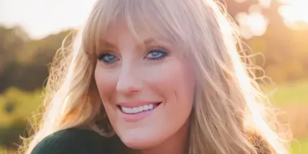 Close-up portrait of a blonde woman smiling outdoors in warm lighting.