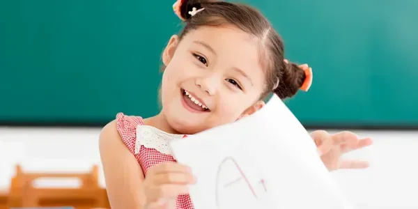 Smiling young girl proudly showing paper with an 'A' grade.