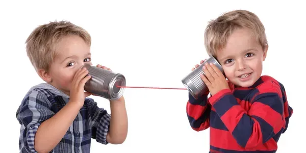 Two young boys playing and talking with a string telephone made of cups.