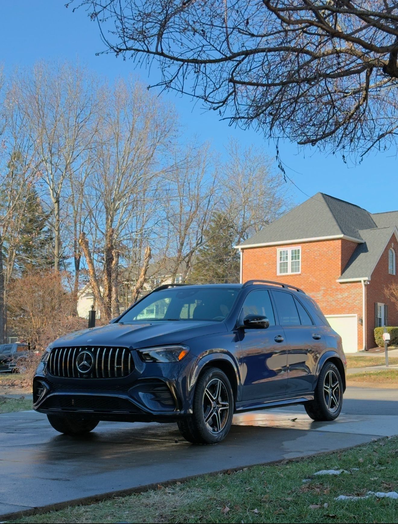 A black car is parked on the side of the road in front of a brick house.