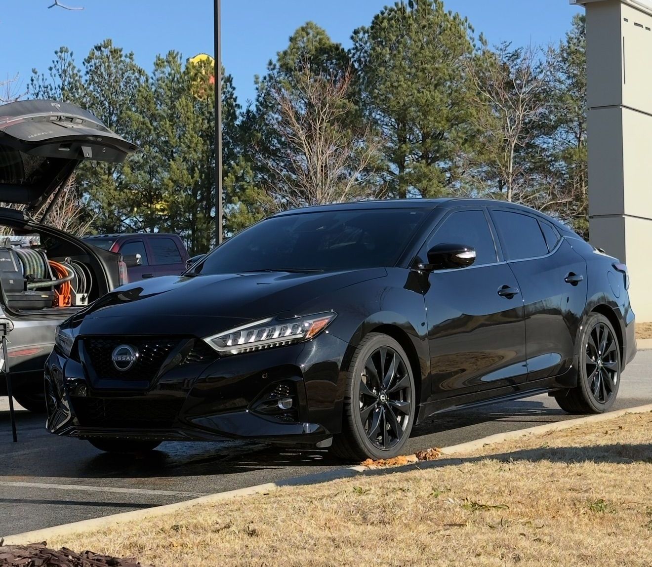 A black car is parked in a parking lot in front of a gas station.