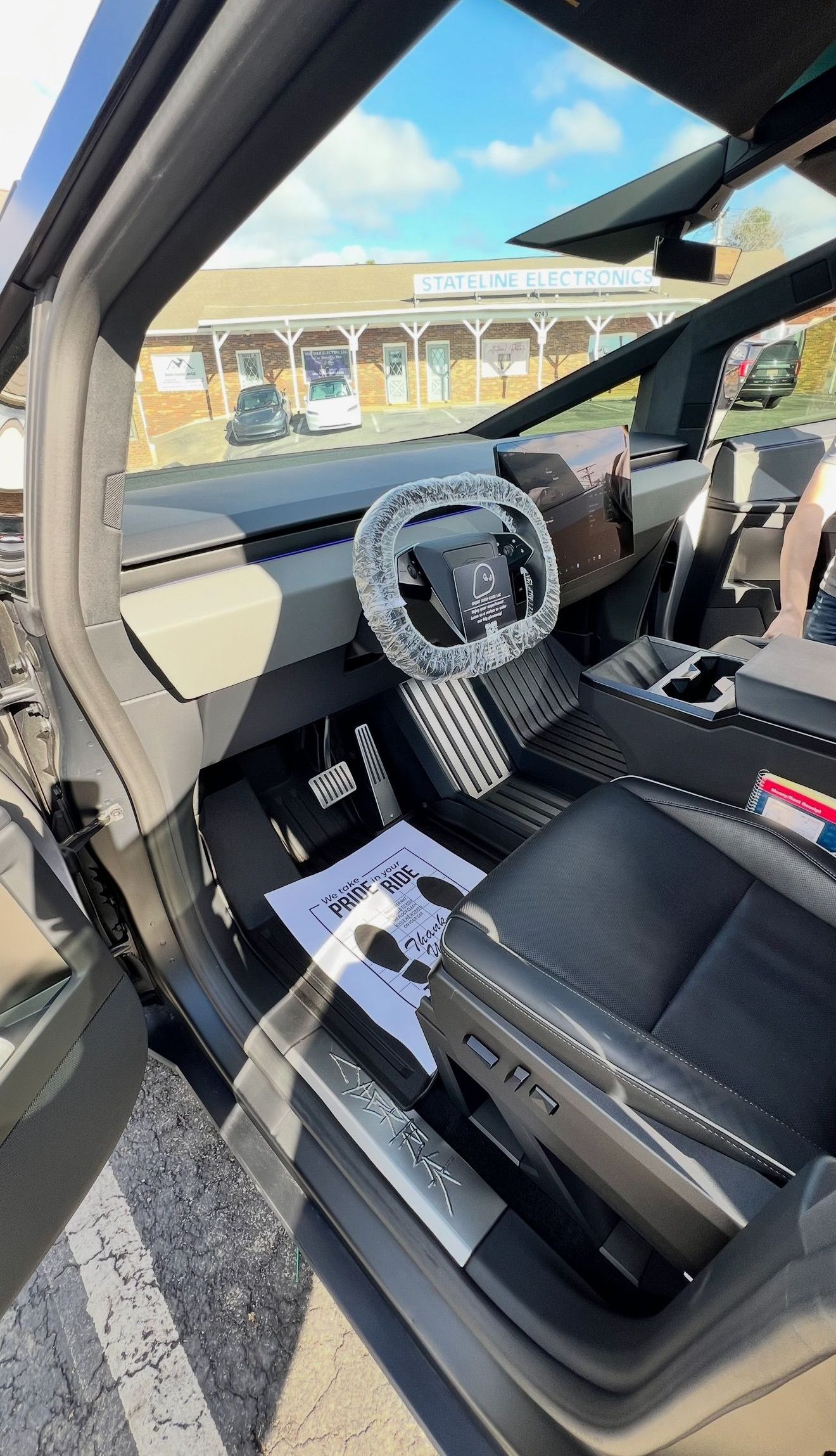 The inside of a tesla model 3 with the door open and the steering wheel visible.