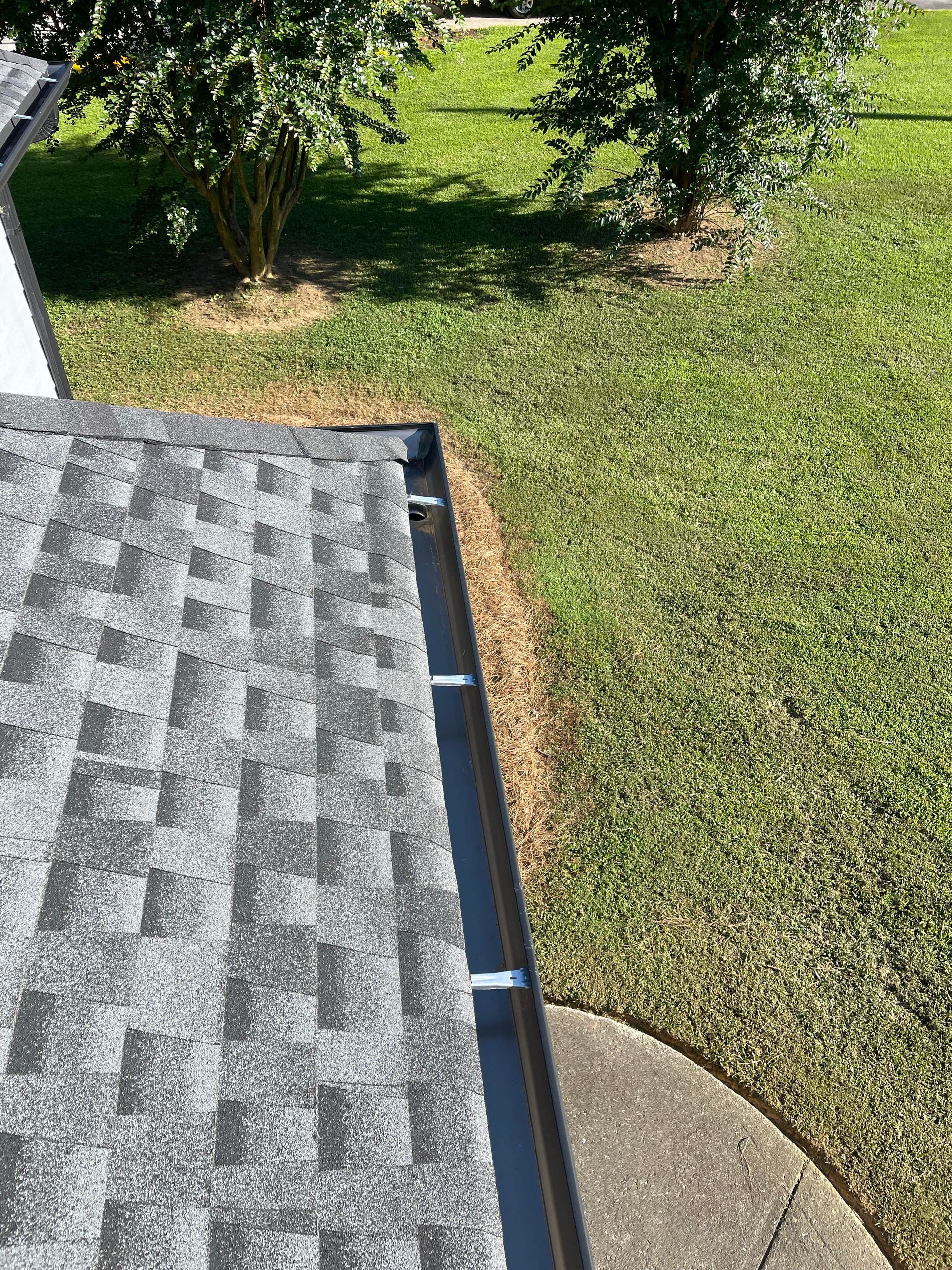 A close up of a gutter on a roof next to a grassy field.