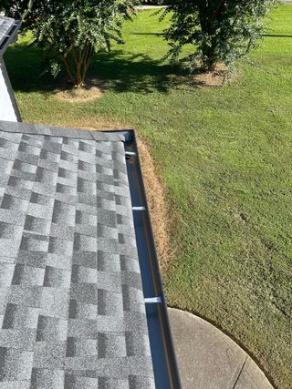 A close up of a gutter on a roof next to a grassy field.