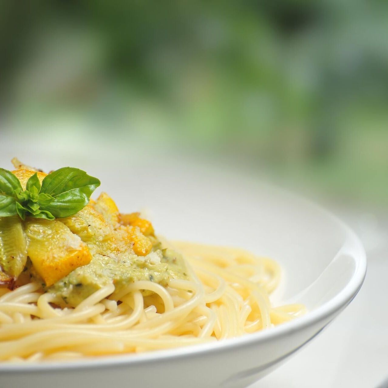 Eine Nahaufnahme einer Schüssel Spaghetti mit Soße und Basilikum auf einem Tisch.