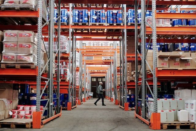 a man is walking through a warehouse filled with lots of shelves .