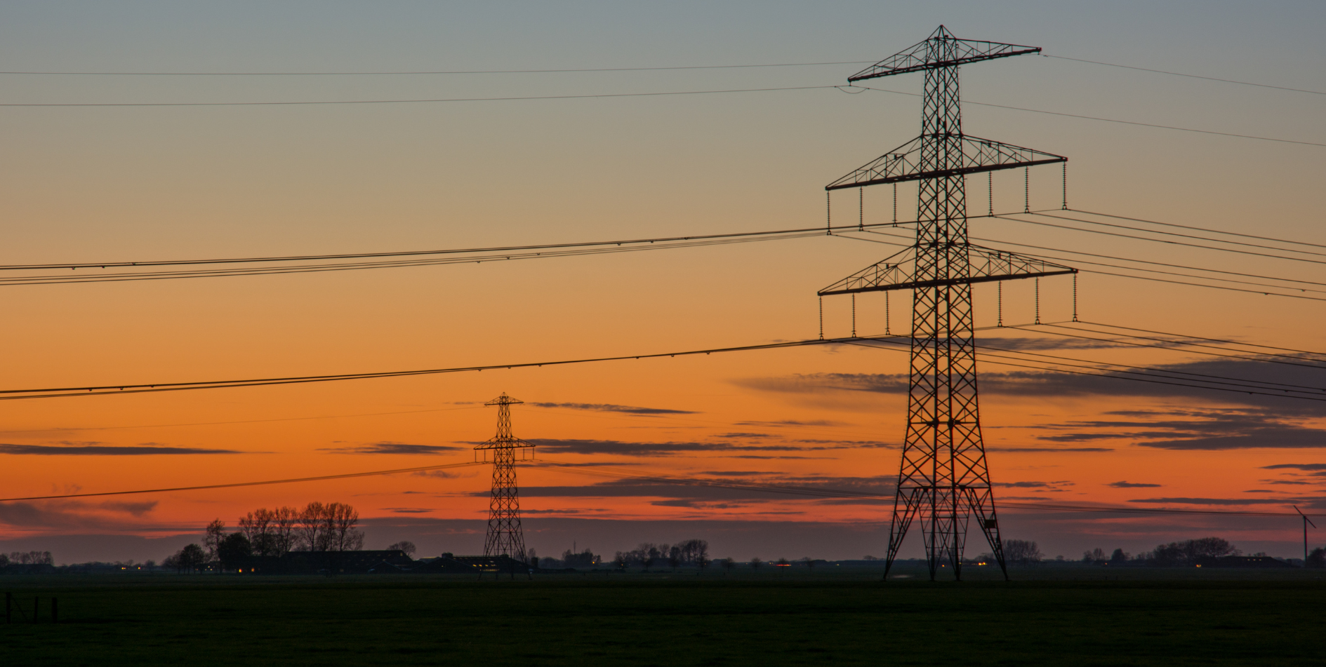 Silhouette of power lines against an orange and blue sunset sky