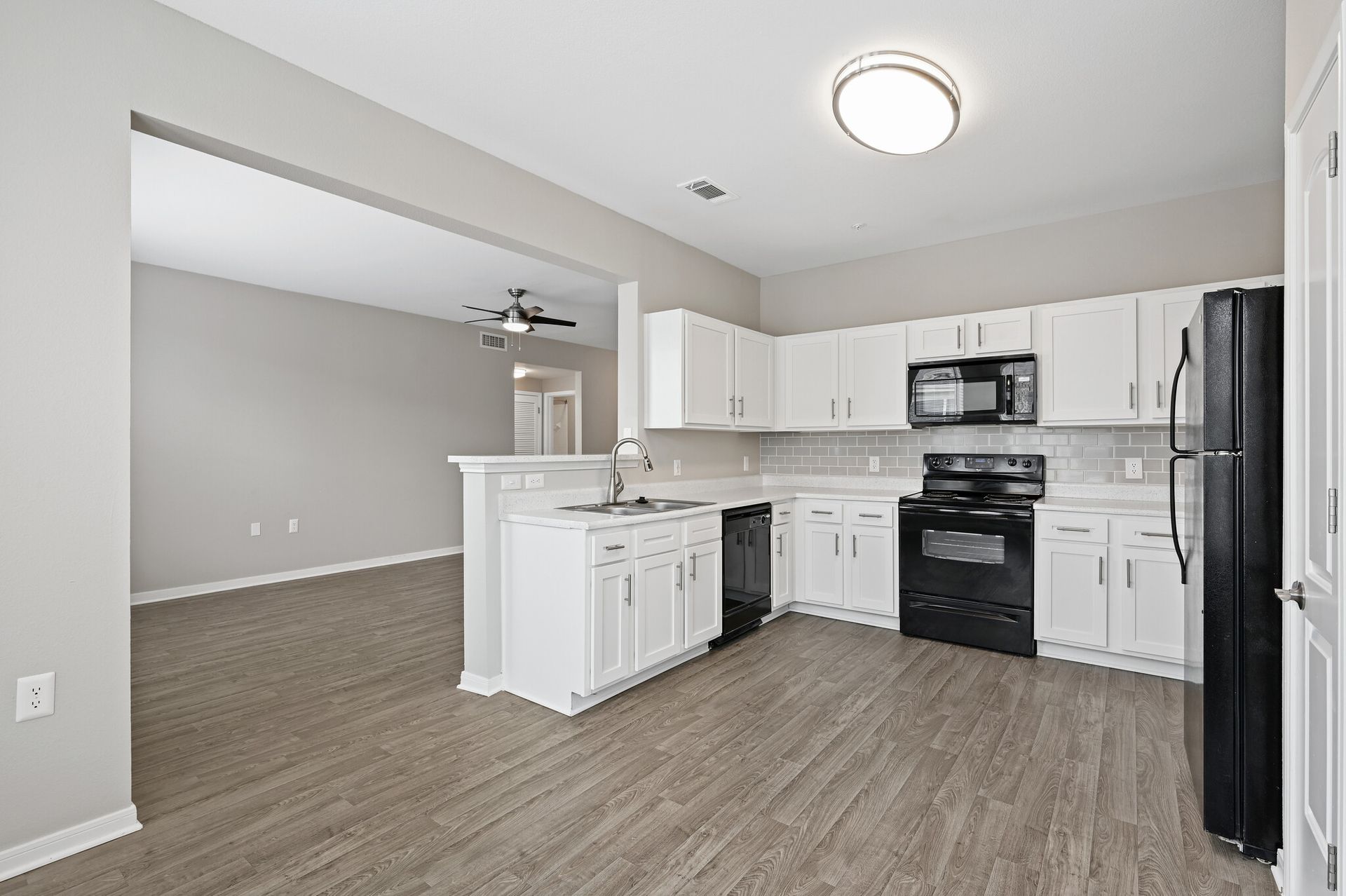A kitchen with white cabinets , a black refrigerator , a stove , and a microwave.
