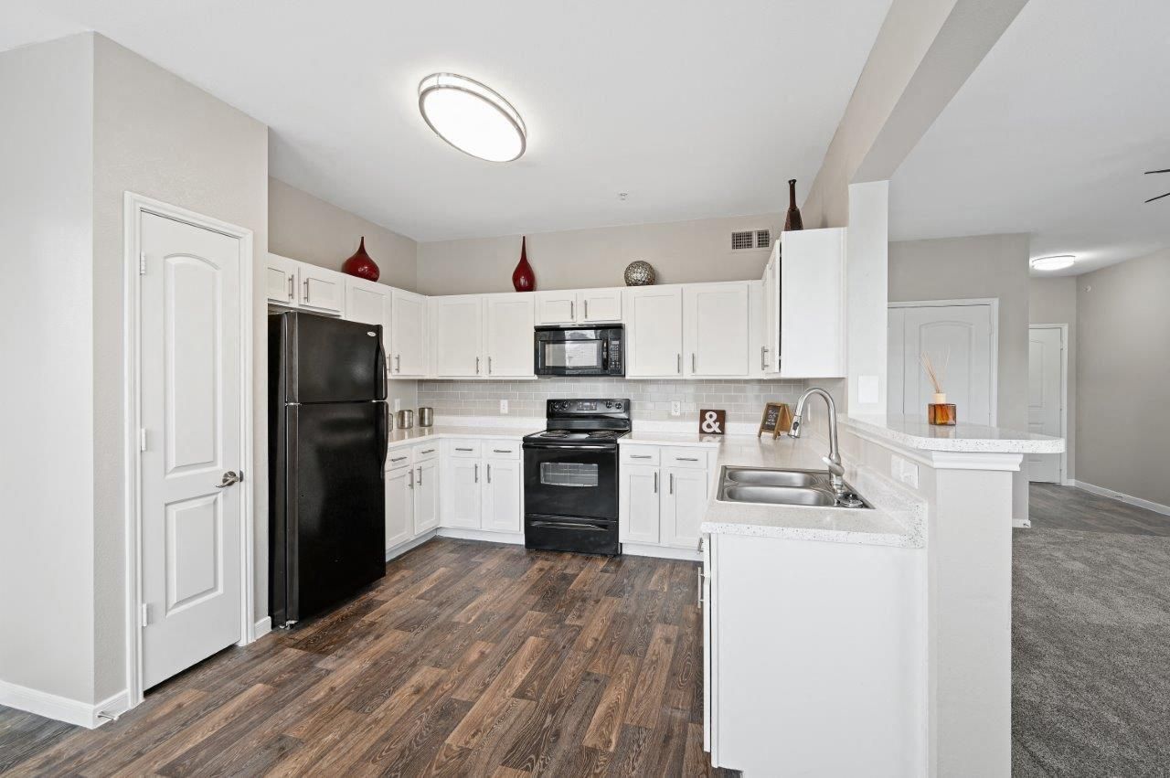 A kitchen with white cabinets , a black refrigerator , a microwave , and a sink.