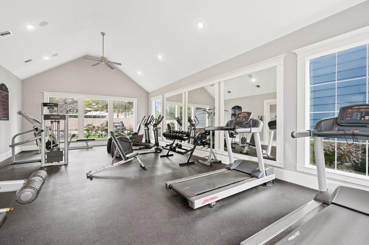 A gym with treadmills , exercise bikes , and a ceiling fan.