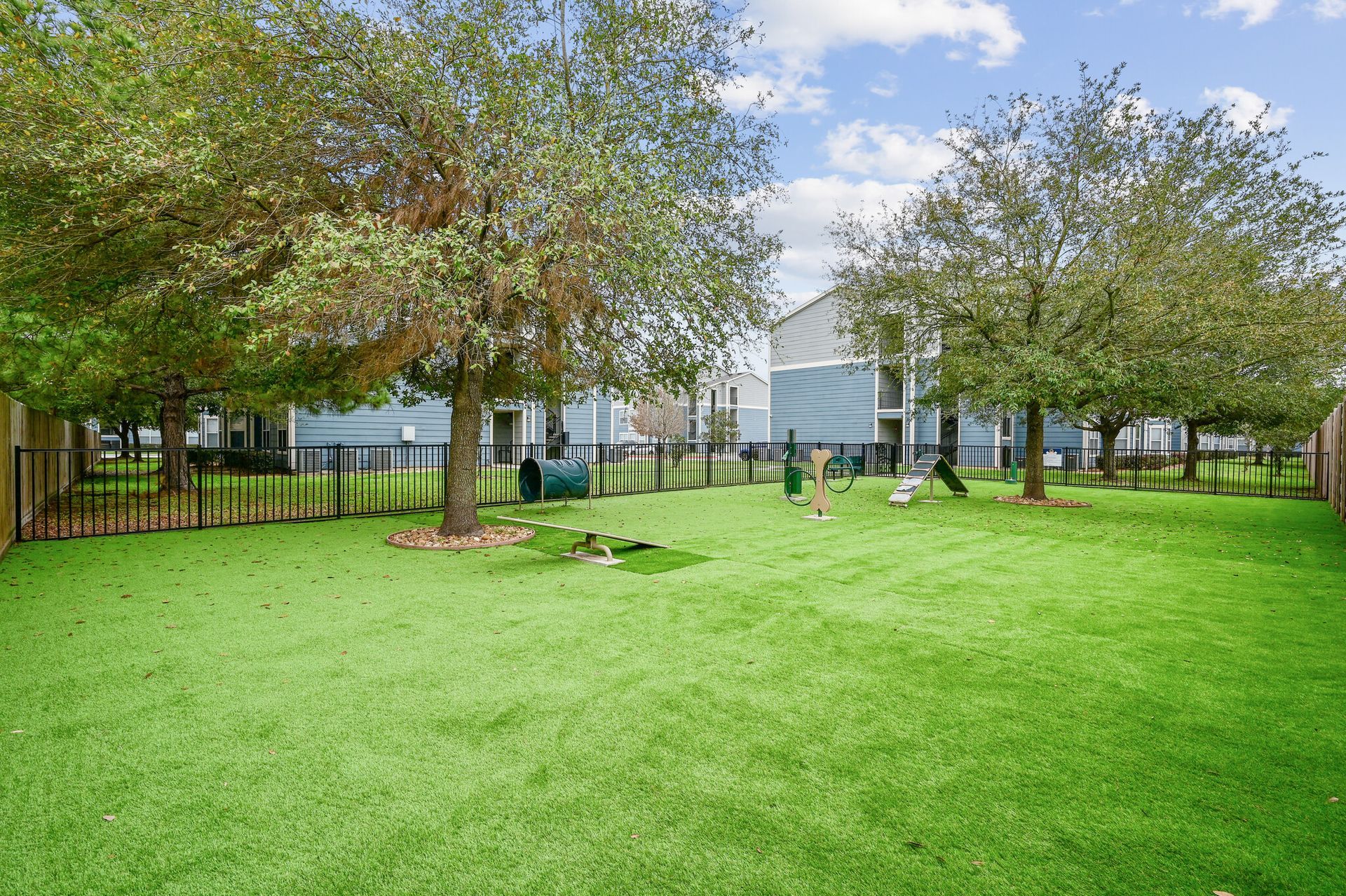 A large lush green yard with a fence and trees in front of a house.