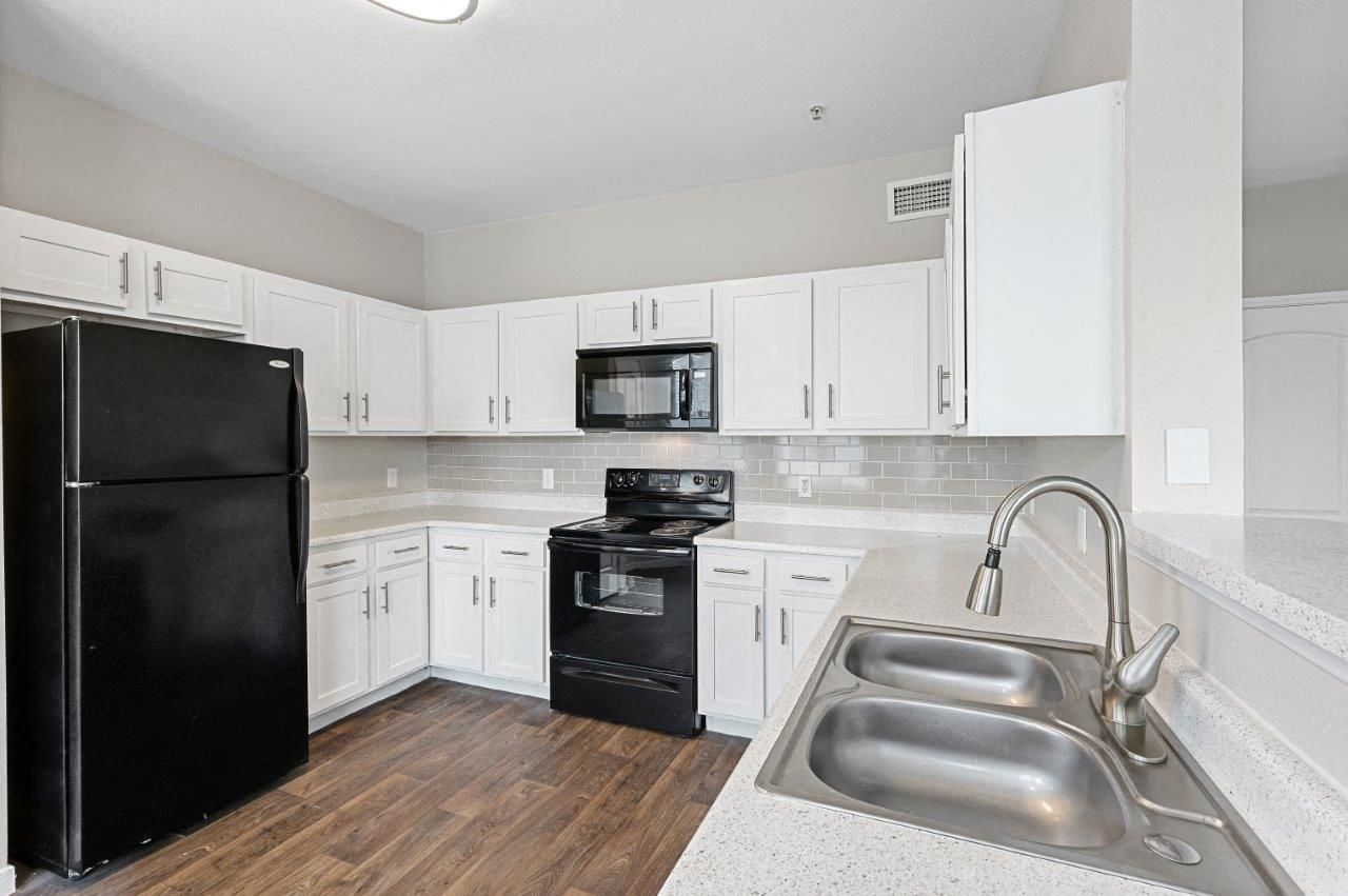 A kitchen with white cabinets , a black refrigerator , a black stove , a microwave and a sink.