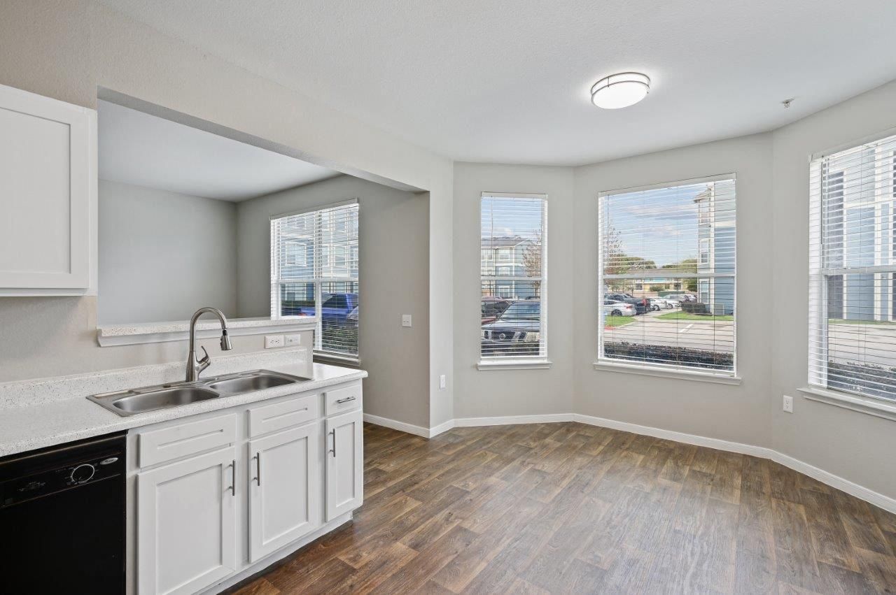 An empty kitchen with white cabinets , a sink , and a dishwasher.