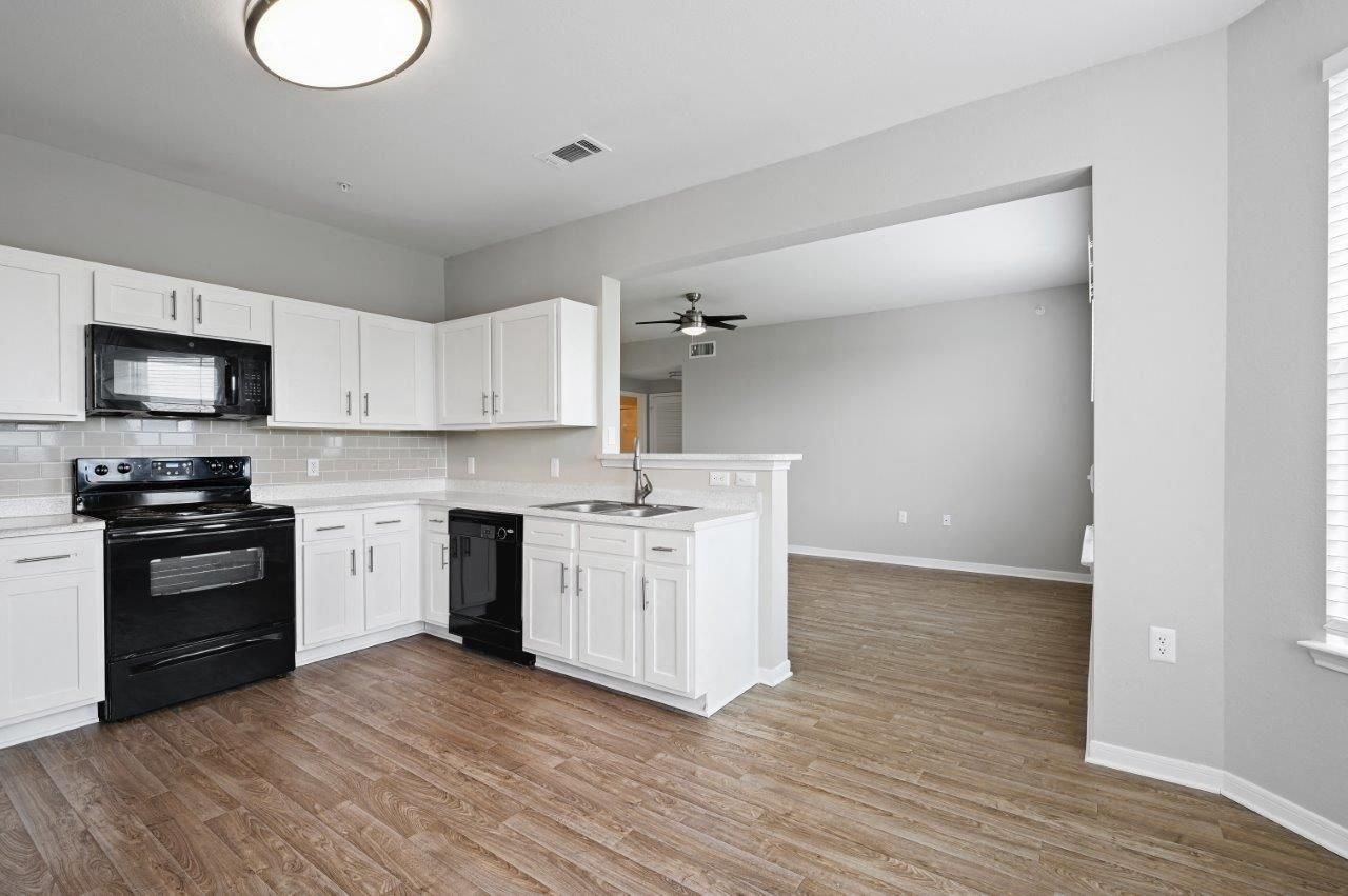 A kitchen with white cabinets , a black stove , a microwave and a ceiling fan.