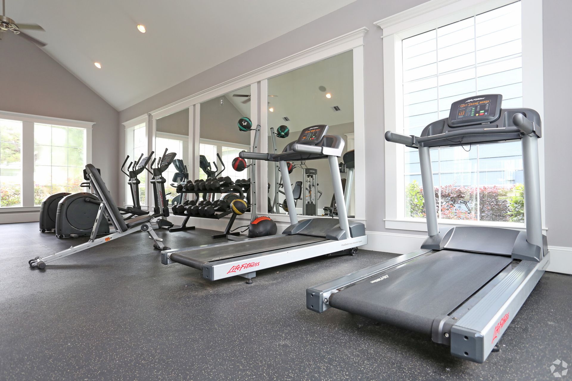 A gym with treadmills , exercise bikes , dumbbells and a mirror.