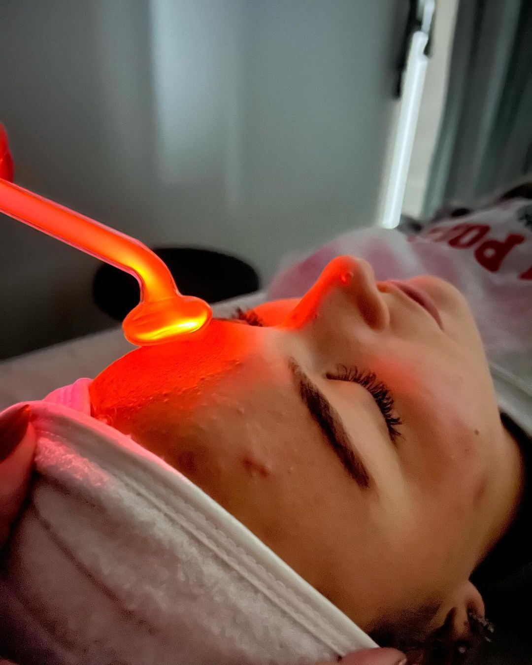 Person receiving high-frequency facial treatment with a glowing orange wand on the forehead.