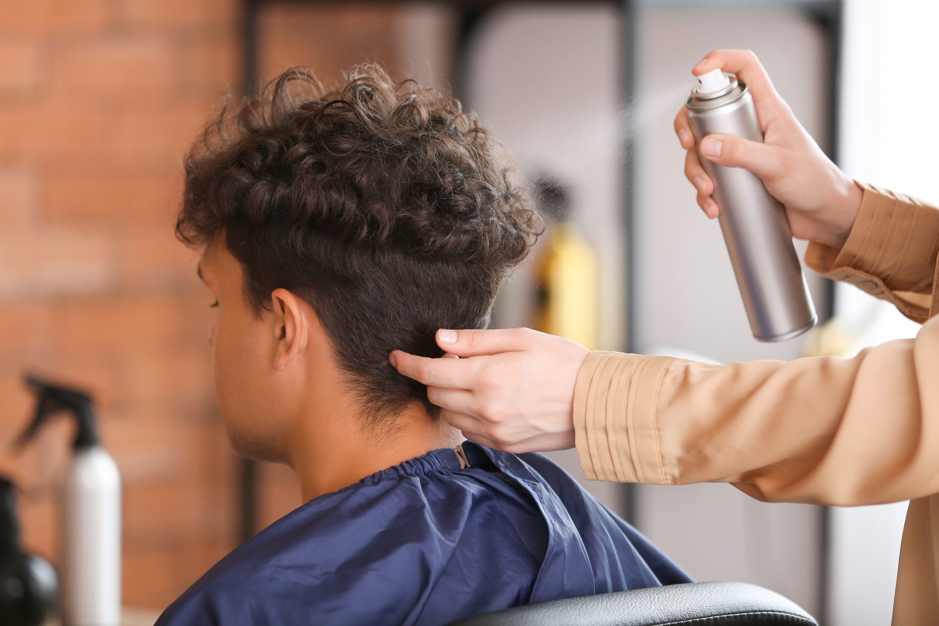 A person's hair being styled with hairspray in a salon.