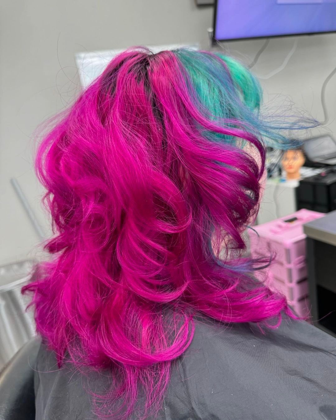 Woman with magenta and teal hair, curled and styled in a salon setting.