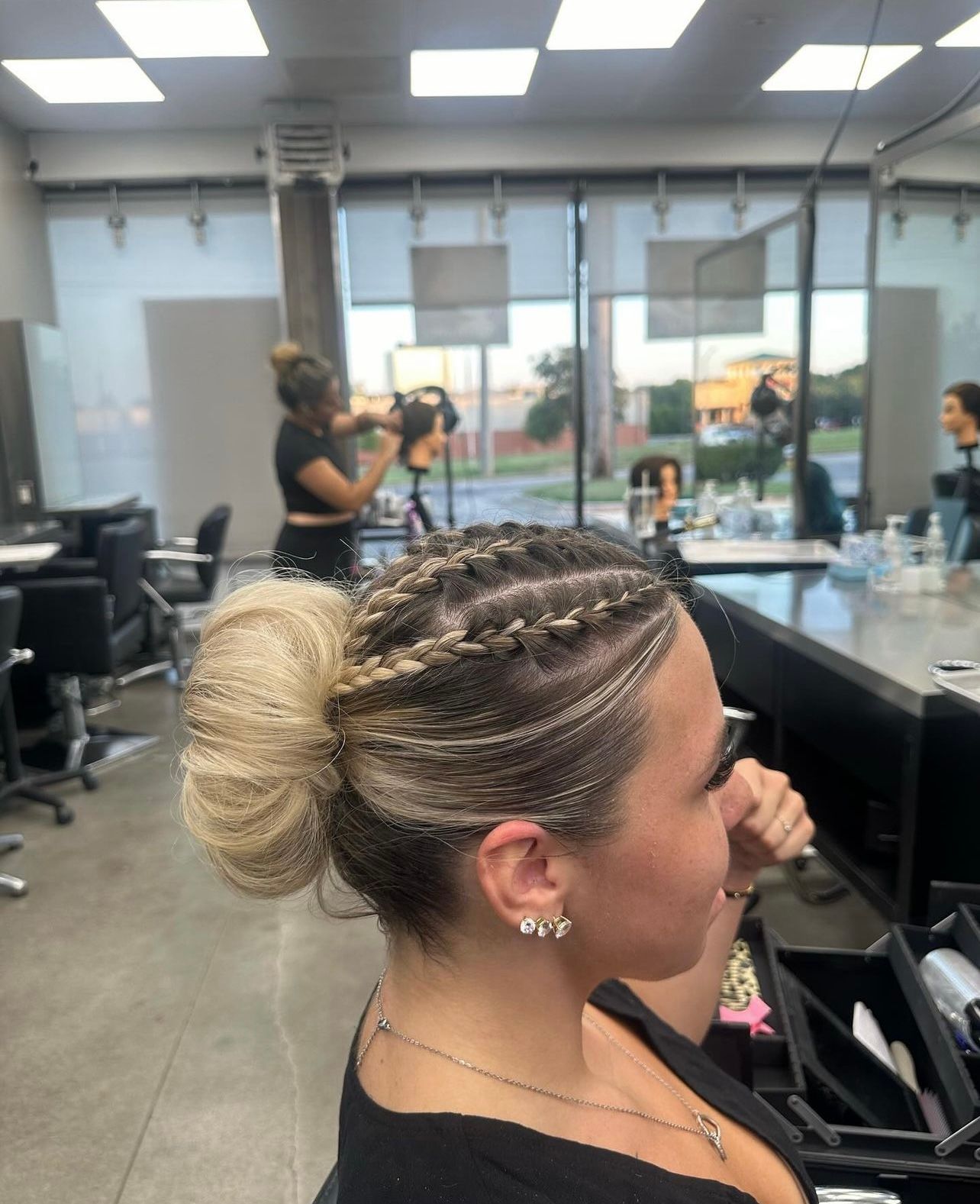 A person in a hair salon with a high blonde bun and braided sections on the side of their head.