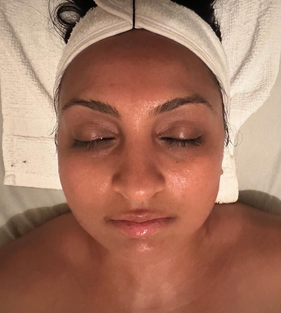 Woman with closed eyes, wearing a white headband, and a towel below her face, appearing relaxed.