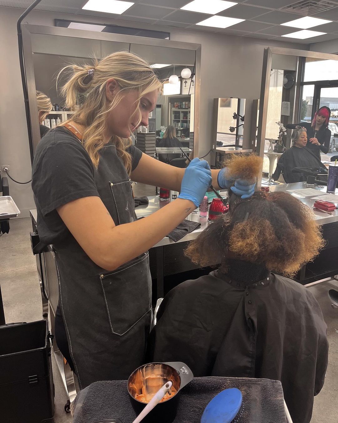 Hairdresser using a hairdryer on client's hair in a salon; client is seated.