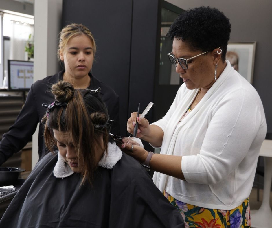 A stylist uses a comb to section hair for a client while an observer watches in a salon setting.