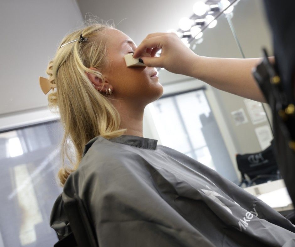 Makeup artist applying foundation to a person's face with a sponge. In a well-lit studio setting.