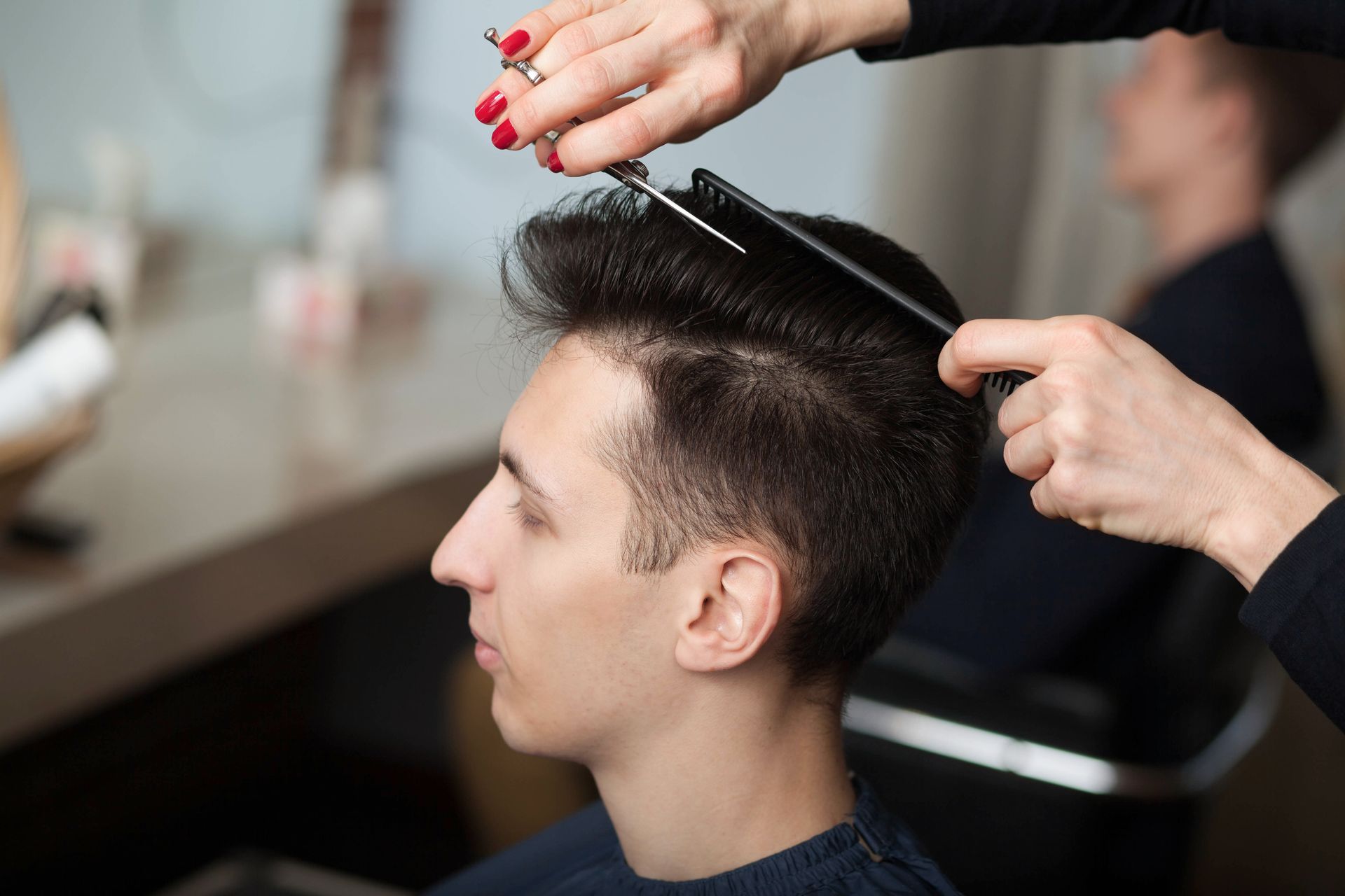 Hair stylist cuts a client's hair with scissors and comb, indoors.